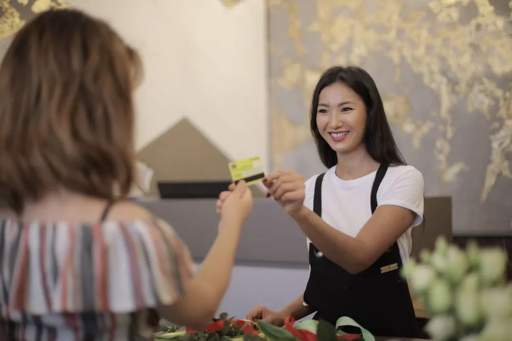 A florist handing a payment card back to a customer across the counter, flowers in the foreground